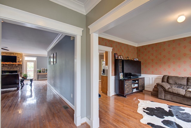 living room with ornamental molding, a stone fireplace, and light wood-type flooring