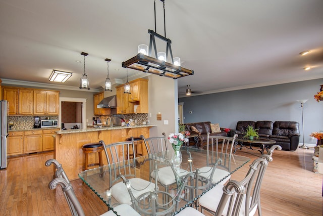 dining area featuring light hardwood / wood-style floors, crown molding, sink, and ceiling fan with notable chandelier