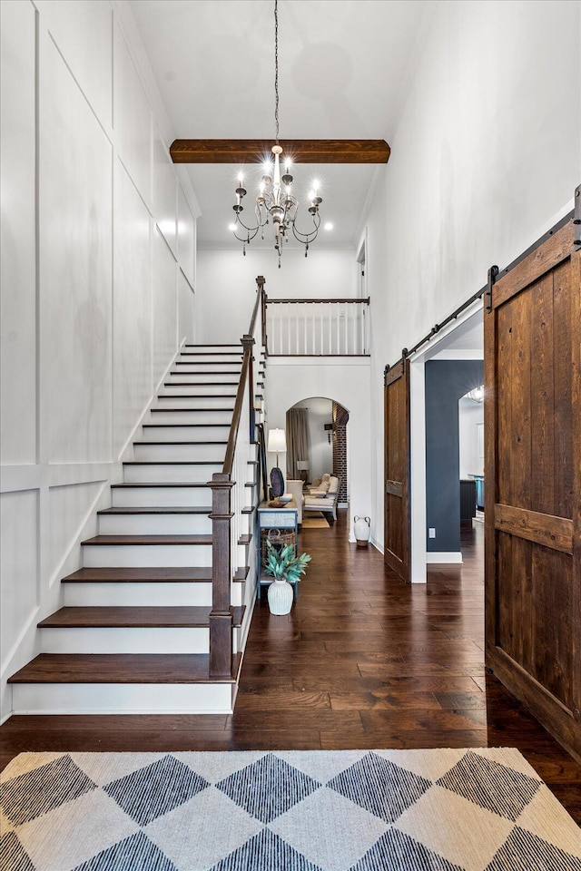 staircase with hardwood / wood-style floors, a barn door, crown molding, a high ceiling, and a notable chandelier