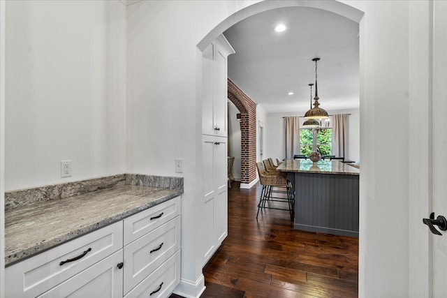 kitchen with light stone countertops, hanging light fixtures, white cabinetry, a breakfast bar area, and dark hardwood / wood-style floors