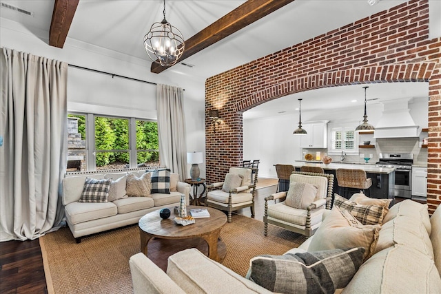 living room with an inviting chandelier, beamed ceiling, brick wall, and dark hardwood / wood-style flooring