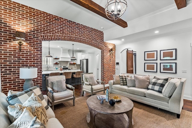 living room with beam ceiling, hardwood / wood-style flooring, a chandelier, and brick wall