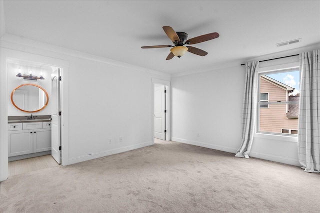 unfurnished bedroom featuring ceiling fan, ornamental molding, ensuite bathroom, sink, and light colored carpet