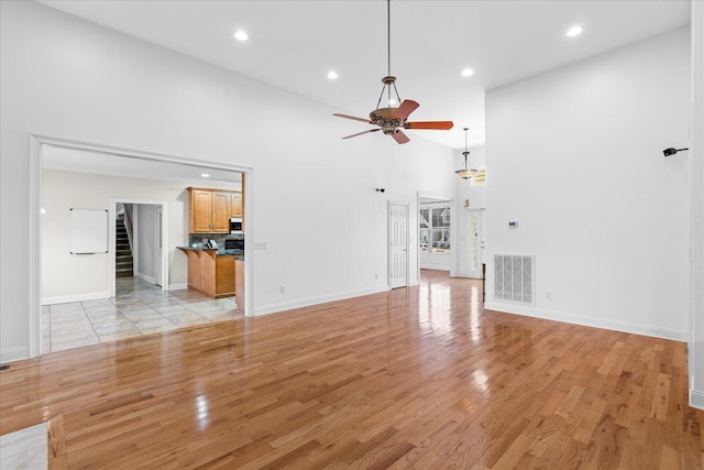 unfurnished living room with light hardwood / wood-style flooring, ceiling fan, and a high ceiling