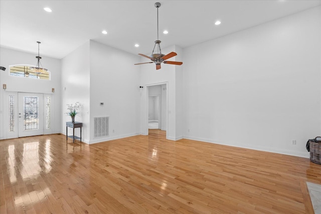 unfurnished living room with ceiling fan, a towering ceiling, and light hardwood / wood-style floors