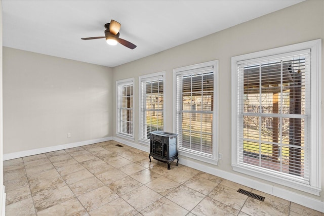 empty room featuring ceiling fan, a wealth of natural light, and a wood stove