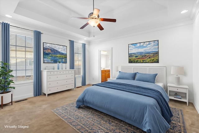 carpeted bedroom featuring ceiling fan, ornamental molding, a raised ceiling, and ensuite bath