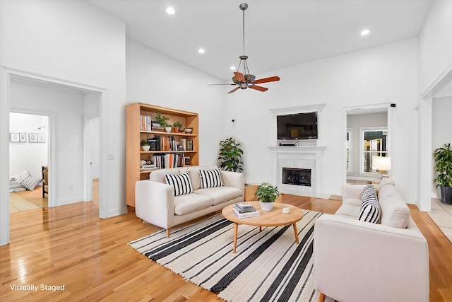 living room with a towering ceiling, light hardwood / wood-style floors, and ceiling fan