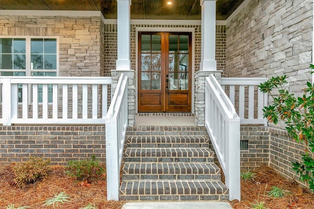 view of exterior entry featuring a porch, french doors, and stone siding