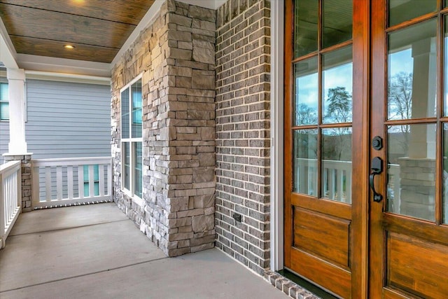 entrance to property with covered porch, brick siding, and french doors