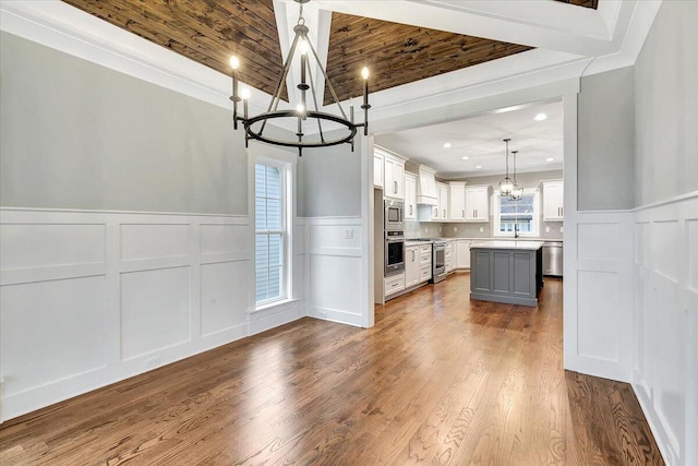 kitchen featuring a kitchen island, appliances with stainless steel finishes, white cabinets, a notable chandelier, and a decorative wall