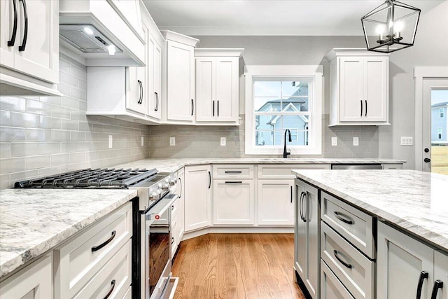 kitchen with high end stove, a sink, custom exhaust hood, light wood finished floors, and white cabinetry