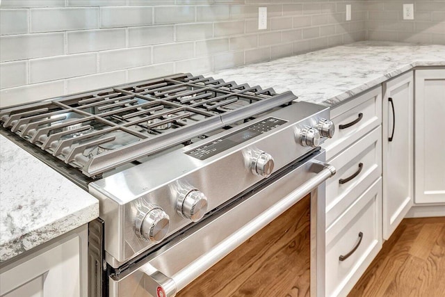 room details featuring decorative backsplash, white cabinets, stainless steel gas range, and light stone countertops