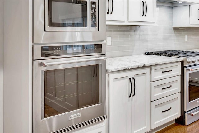 kitchen featuring light stone countertops, stainless steel appliances, white cabinetry, decorative backsplash, and wood finished floors