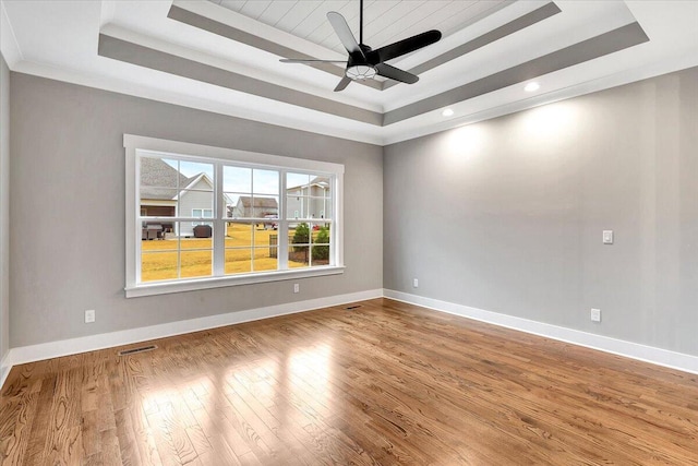 empty room with visible vents, wood finished floors, baseboards, a tray ceiling, and a ceiling fan