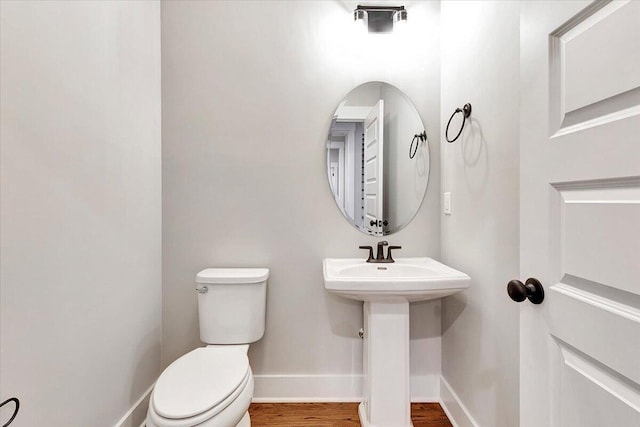 half bathroom featuring baseboards, wood finished floors, and toilet