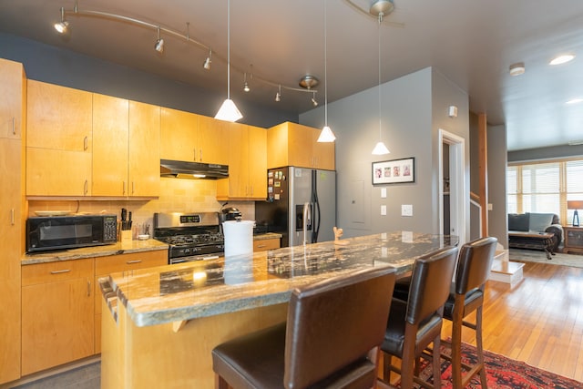 kitchen with appliances with stainless steel finishes, a breakfast bar, light wood-type flooring, and pendant lighting