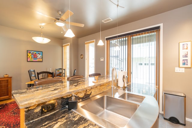 kitchen with hanging light fixtures, light stone countertops, a kitchen bar, and ceiling fan