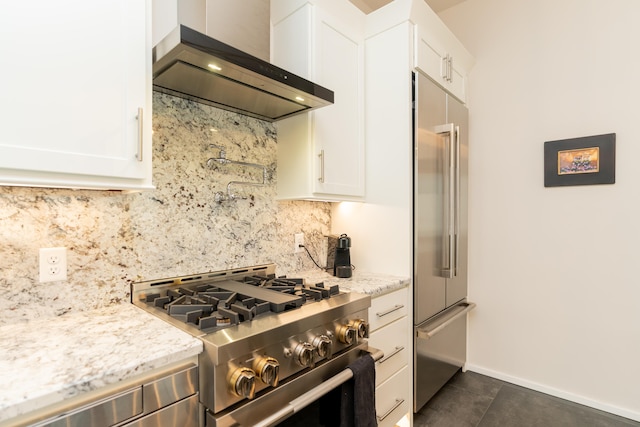 kitchen featuring light stone counters, premium appliances, wall chimney exhaust hood, and white cabinets