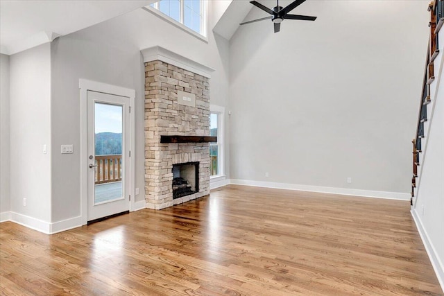 unfurnished living room with ceiling fan, a stone fireplace, light hardwood / wood-style flooring, and a high ceiling