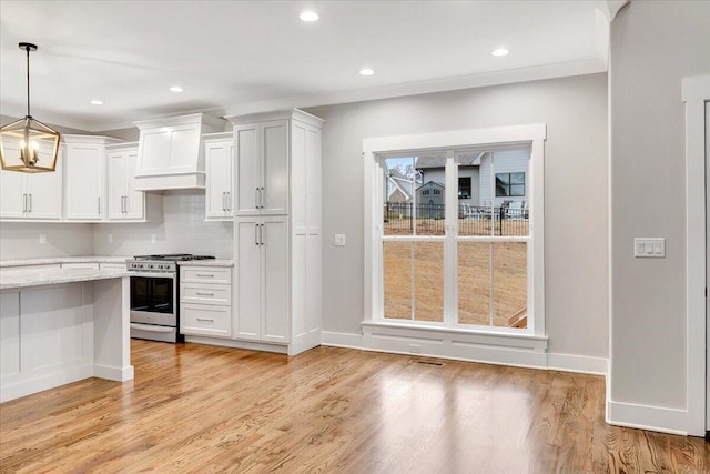 kitchen featuring stainless steel range with gas stovetop, white cabinetry, decorative light fixtures, custom exhaust hood, and light hardwood / wood-style flooring