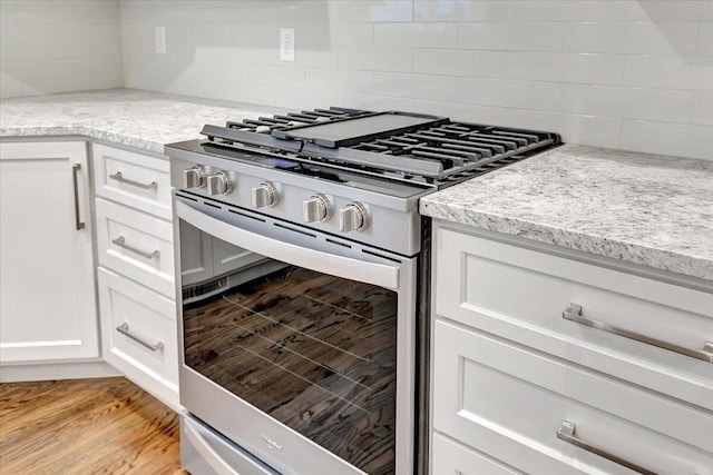 kitchen with high end stove, light stone countertops, white cabinetry, and light wood-type flooring