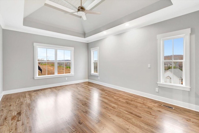 empty room with hardwood / wood-style floors, ceiling fan, and a raised ceiling