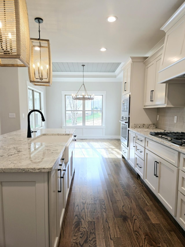 kitchen with dark wood-type flooring, an island with sink, decorative light fixtures, white cabinets, and appliances with stainless steel finishes