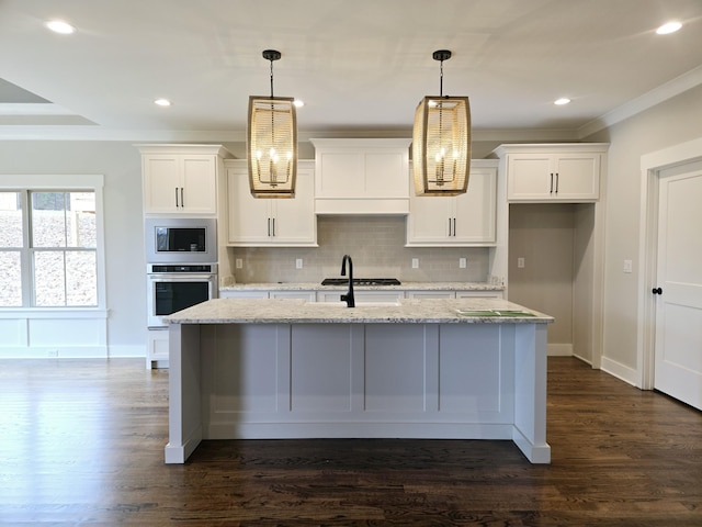 kitchen with white cabinets, decorative light fixtures, a center island with sink, and stainless steel appliances