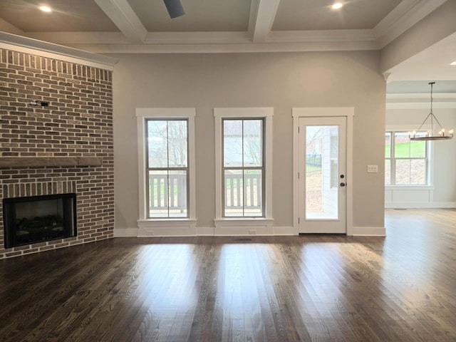 unfurnished living room featuring an inviting chandelier, beam ceiling, dark hardwood / wood-style flooring, and a brick fireplace