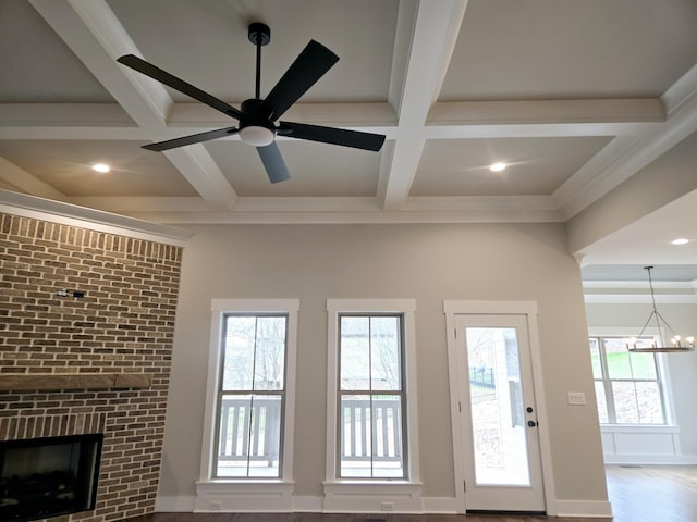 unfurnished living room with plenty of natural light, coffered ceiling, ceiling fan with notable chandelier, and a brick fireplace