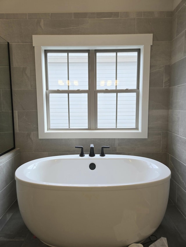 bathroom featuring a bathing tub, a healthy amount of sunlight, and tile walls