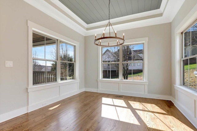 unfurnished dining area featuring hardwood / wood-style flooring, an inviting chandelier, ornamental molding, wooden ceiling, and a raised ceiling