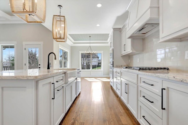 kitchen with hanging light fixtures, a tray ceiling, stainless steel appliances, and white cabinets