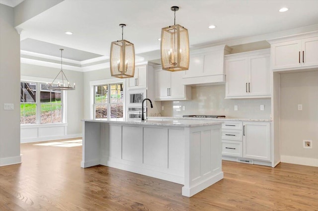 kitchen with white cabinetry, a kitchen island with sink, light hardwood / wood-style floors, and decorative light fixtures