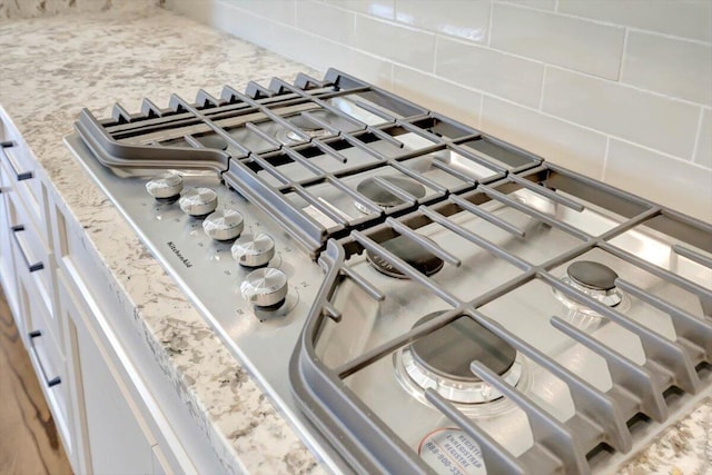 room details featuring light stone counters, stainless steel gas cooktop, and backsplash