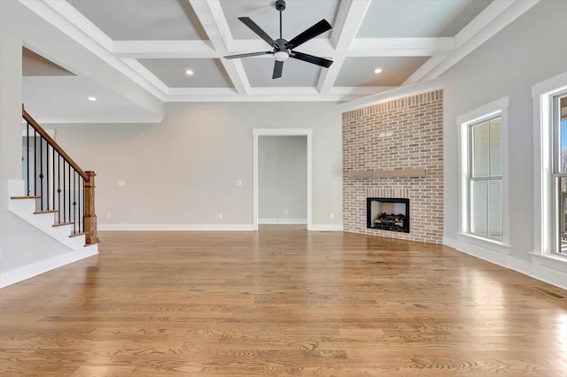 unfurnished living room featuring ceiling fan, beam ceiling, a brick fireplace, and light hardwood / wood-style flooring