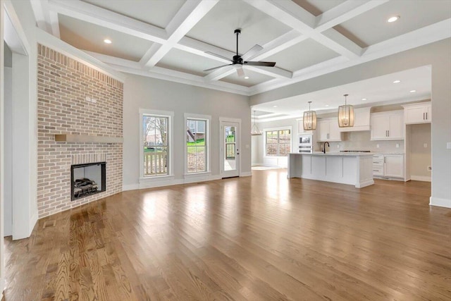 unfurnished living room featuring sink, a brick fireplace, light wood-type flooring, beamed ceiling, and ceiling fan