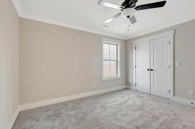 unfurnished bedroom featuring ceiling fan, light colored carpet, ornamental molding, and a closet