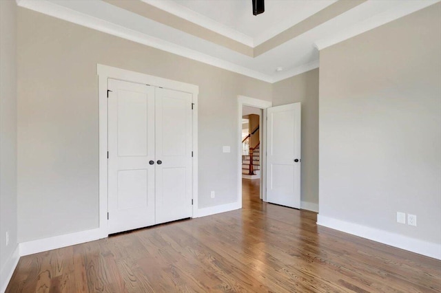 unfurnished bedroom featuring crown molding, ceiling fan, hardwood / wood-style floors, a tray ceiling, and a closet