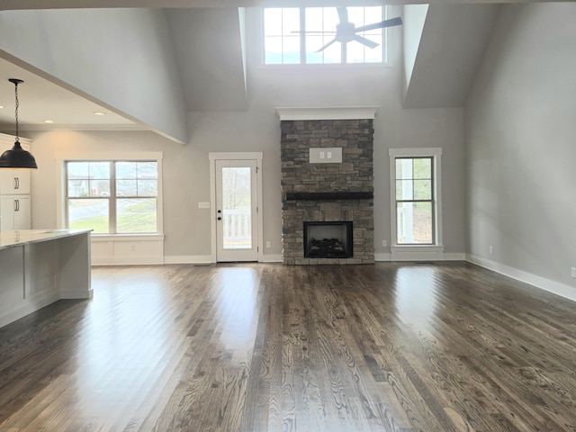 unfurnished living room with a stone fireplace, dark hardwood / wood-style floors, ceiling fan, and a high ceiling