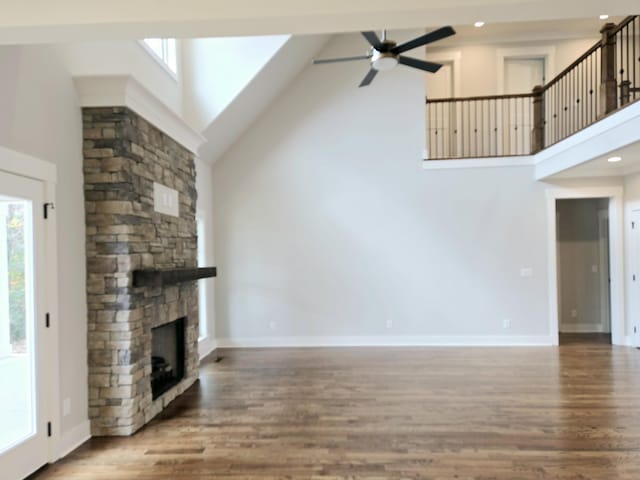 unfurnished living room with a fireplace, plenty of natural light, high vaulted ceiling, and wood-type flooring