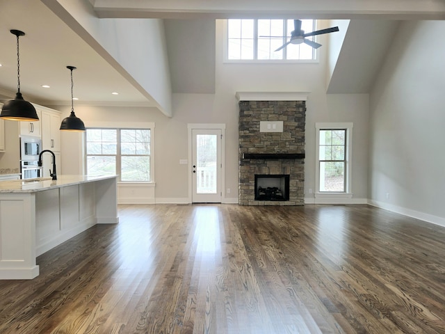 unfurnished living room featuring dark hardwood / wood-style flooring, a stone fireplace, a towering ceiling, and ceiling fan