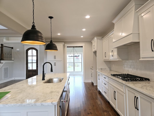 kitchen featuring sink, a kitchen island with sink, hanging light fixtures, light stone counters, and white cabinets