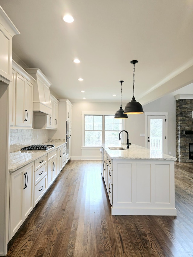 kitchen featuring pendant lighting, sink, appliances with stainless steel finishes, white cabinetry, and a center island with sink