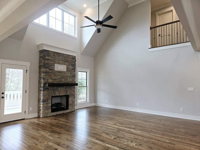 unfurnished living room with a stone fireplace, dark wood-type flooring, ceiling fan, and a high ceiling