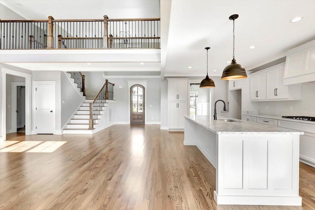 kitchen with sink, hanging light fixtures, light stone countertops, a large island with sink, and light wood-type flooring