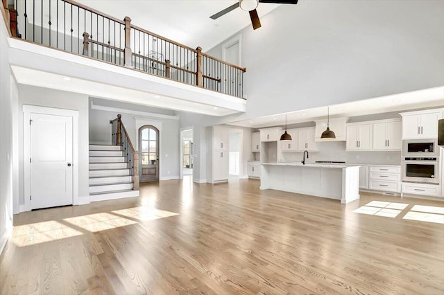 unfurnished living room featuring sink, a towering ceiling, light hardwood / wood-style floors, and ceiling fan