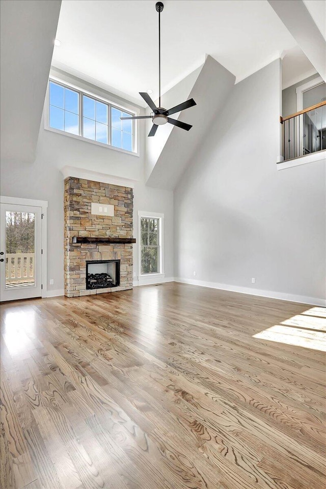 unfurnished living room with a high ceiling, ceiling fan, a stone fireplace, and light hardwood / wood-style floors