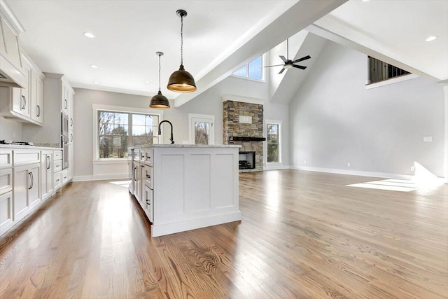 kitchen featuring decorative light fixtures, light wood-type flooring, an island with sink, a fireplace, and white cabinets